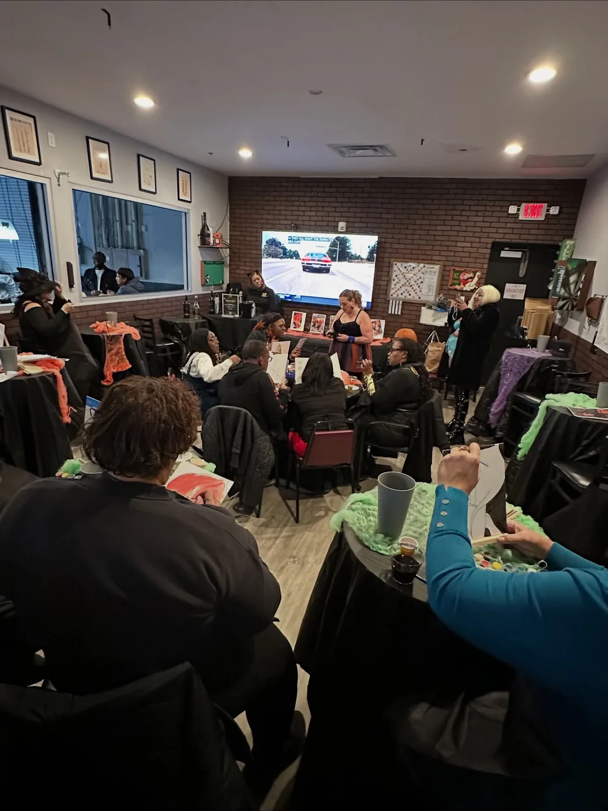Guests seated at dressed tables in the private event room, watching a screen at a hosted party.